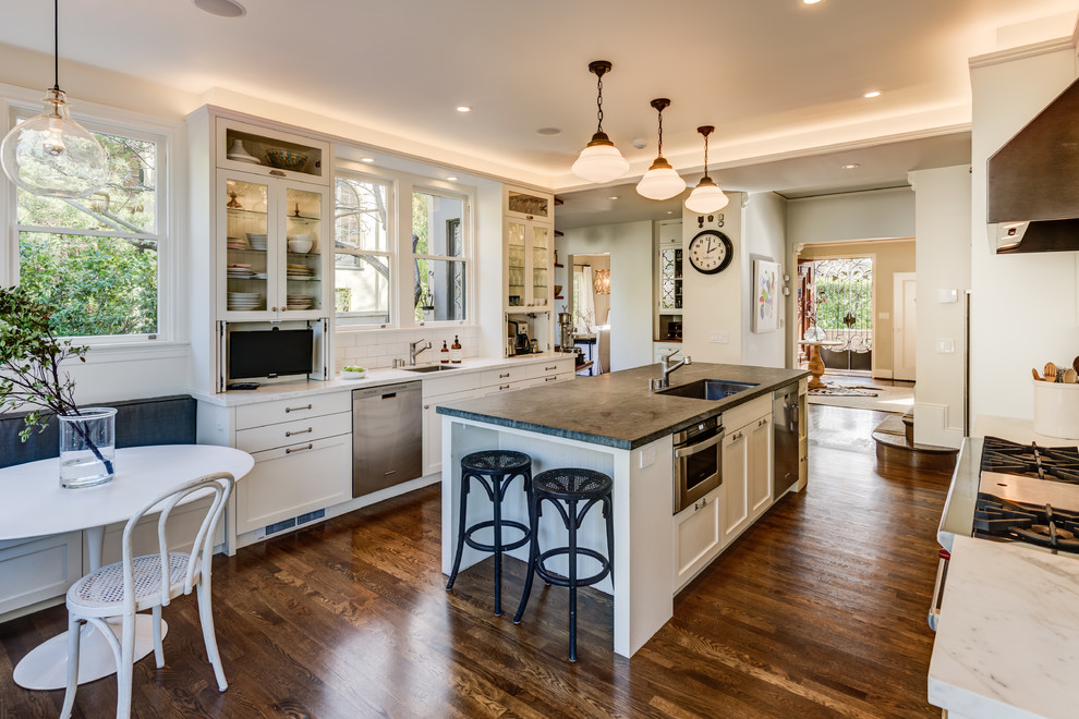 This is an example of a large traditional galley eat-in kitchen in San Francisco with an undermount sink, glass-front cabinets, white cabinets, white splashback, subway tile splashback, stainless steel appliances, dark hardwood floors, with island, soapstone benchtops, brown floor and black benchtop.