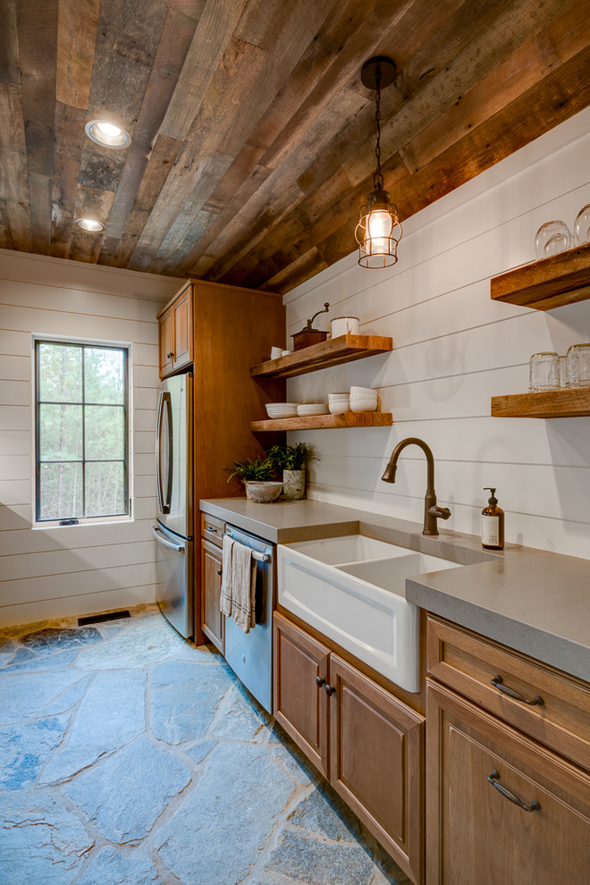 This is an example of a mid-sized country galley separate kitchen in Other with a farmhouse sink, raised-panel cabinets, medium wood cabinets, quartz benchtops, stainless steel appliances, slate floors and no island.