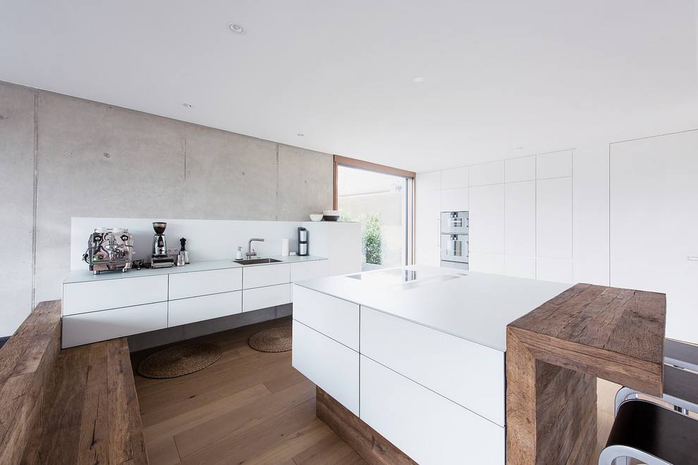 Industrial galley separate kitchen in Munich with flat-panel cabinets, white cabinets, white splashback, stainless steel appliances, dark hardwood floors, with island and brown floor.