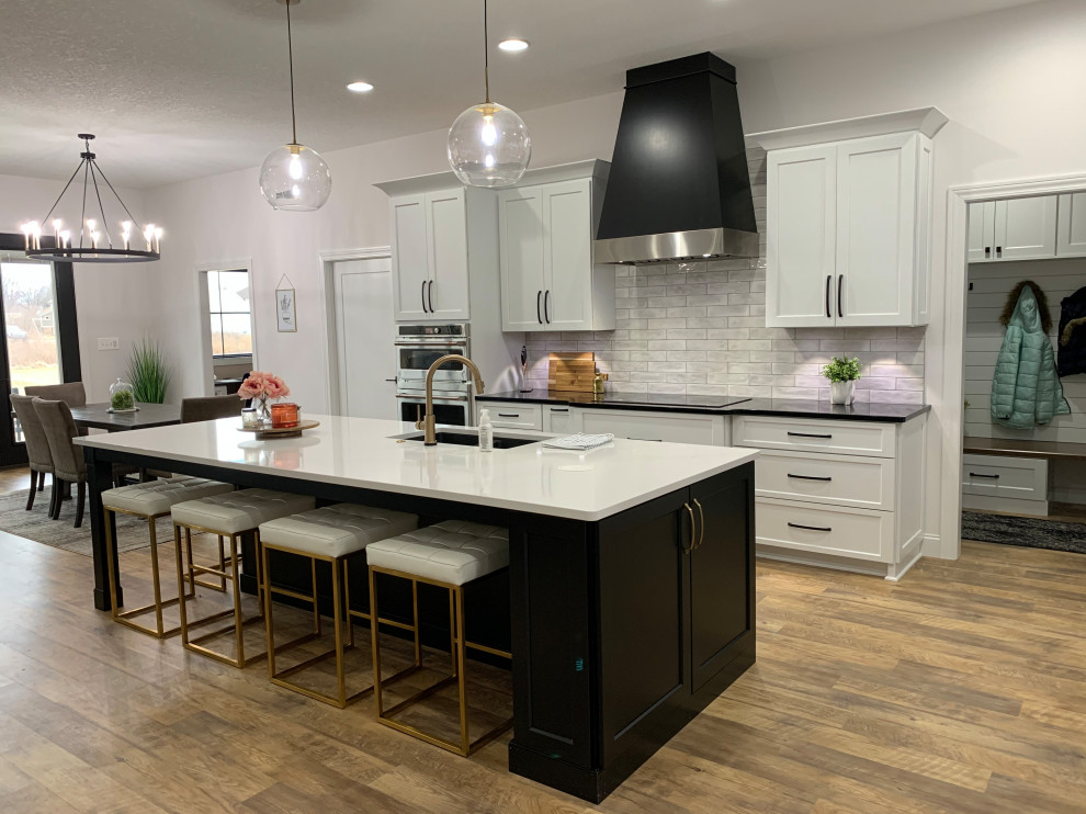 Large transitional l-shaped vinyl floor and brown floor open concept kitchen photo with an undermount sink, recessed-panel cabinets, white cabinets, quartz countertops, white backsplash, ceramic backsplash, stainless steel appliances, an island and white countertops