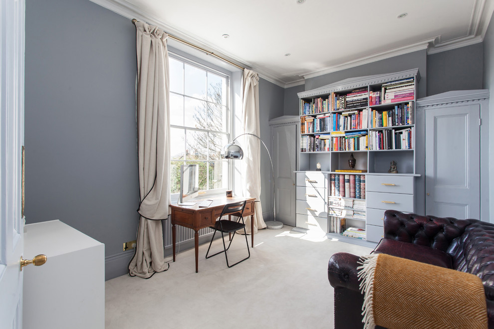 Photo of a mid-sized transitional home office in London with blue walls, carpet, a freestanding desk and white floor.