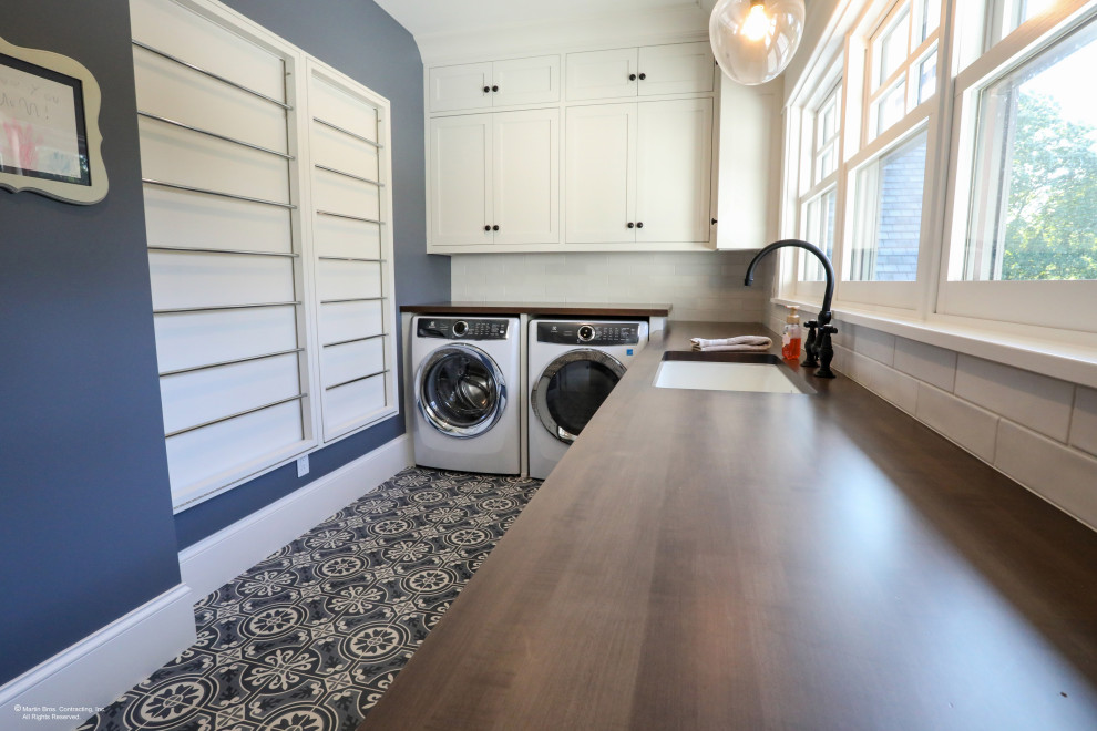 Design ideas for a large transitional u-shaped dedicated laundry room in Other with a farmhouse sink, shaker cabinets, white cabinets, wood benchtops, white splashback, ceramic splashback, blue walls, ceramic floors, an integrated washer and dryer and grey floor.