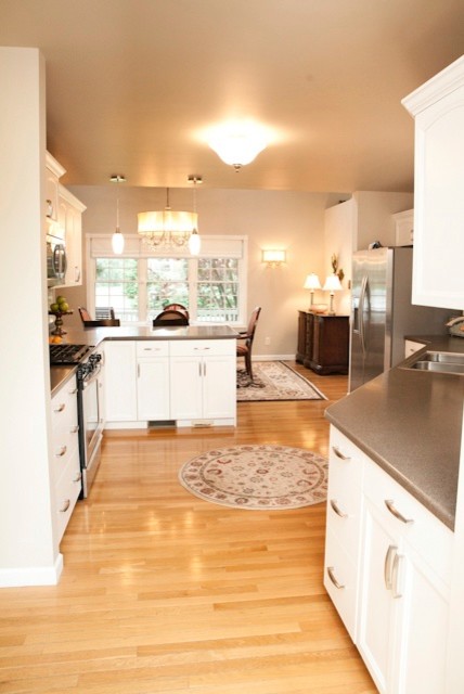 Eat-in kitchen - mid-sized transitional u-shaped light wood floor eat-in kitchen idea in Charlotte with white cabinets, white backsplash, stainless steel appliances, a peninsula, a double-bowl sink, shaker cabinets, solid surface countertops and stone tile backsplash