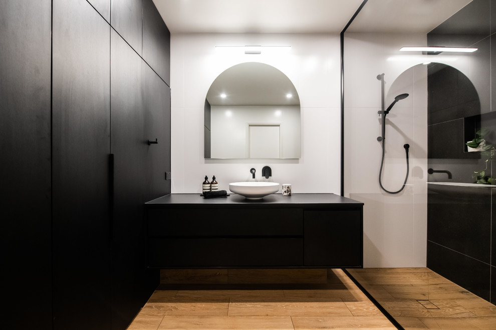 Design ideas for a large contemporary bathroom in Melbourne with an open shower, white tile, ceramic tile, black walls, porcelain floors, a vessel sink, brown floor, an open shower, black benchtops, furniture-like cabinets, black cabinets and glass benchtops.