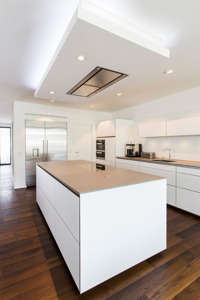 Contemporary l-shaped open plan kitchen in Bremen with an integrated sink, flat-panel cabinets, white cabinets, stainless steel appliances, dark hardwood floors, multiple islands and brown floor.