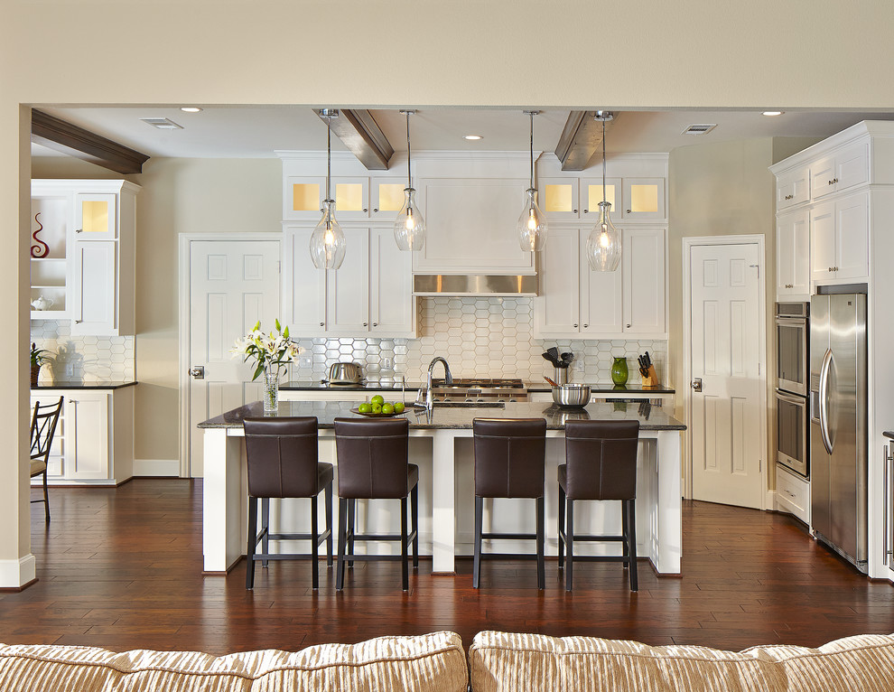 This is an example of a transitional l-shaped kitchen in Dallas with shaker cabinets, white cabinets, white splashback, stainless steel appliances, dark hardwood floors and with island.