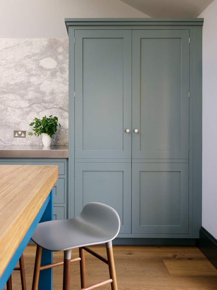Design ideas for a large traditional u-shaped enclosed kitchen in London with a submerged sink, recessed-panel cabinets, blue cabinets, composite countertops, grey splashback, stone slab splashback, stainless steel appliances, medium hardwood flooring, an island and brown floors.