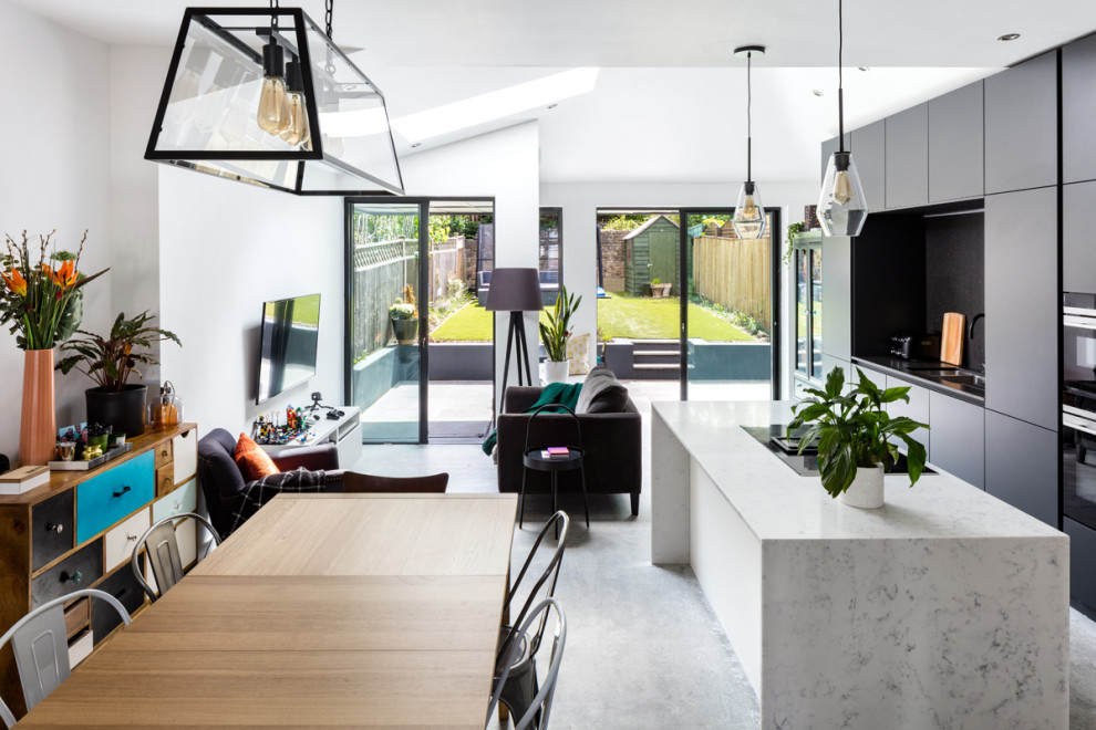 Photo of a mid-sized contemporary galley eat-in kitchen in London with a single-bowl sink, recessed-panel cabinets, black cabinets, marble benchtops, black splashback, slate splashback, black appliances, concrete floors, with island, grey floor and white benchtop.
