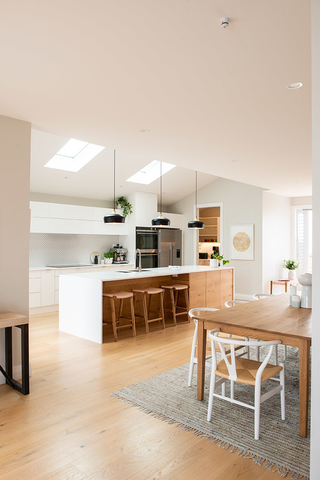 Inspiration for a scandinavian galley eat-in kitchen in Auckland with white cabinets, white splashback, ceramic splashback, stainless steel appliances, light hardwood floors, with island and beige floor.