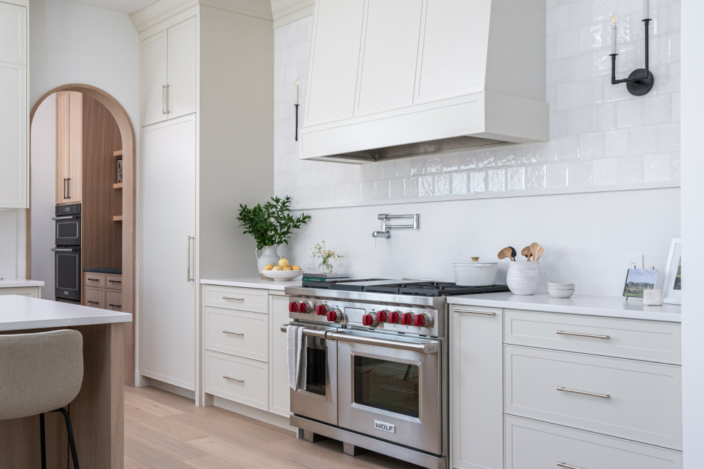 Inspiration for a large transitional l-shaped light wood floor kitchen remodel with shaker cabinets, quartz countertops, white backsplash, quartz backsplash, stainless steel appliances, an island and white countertops