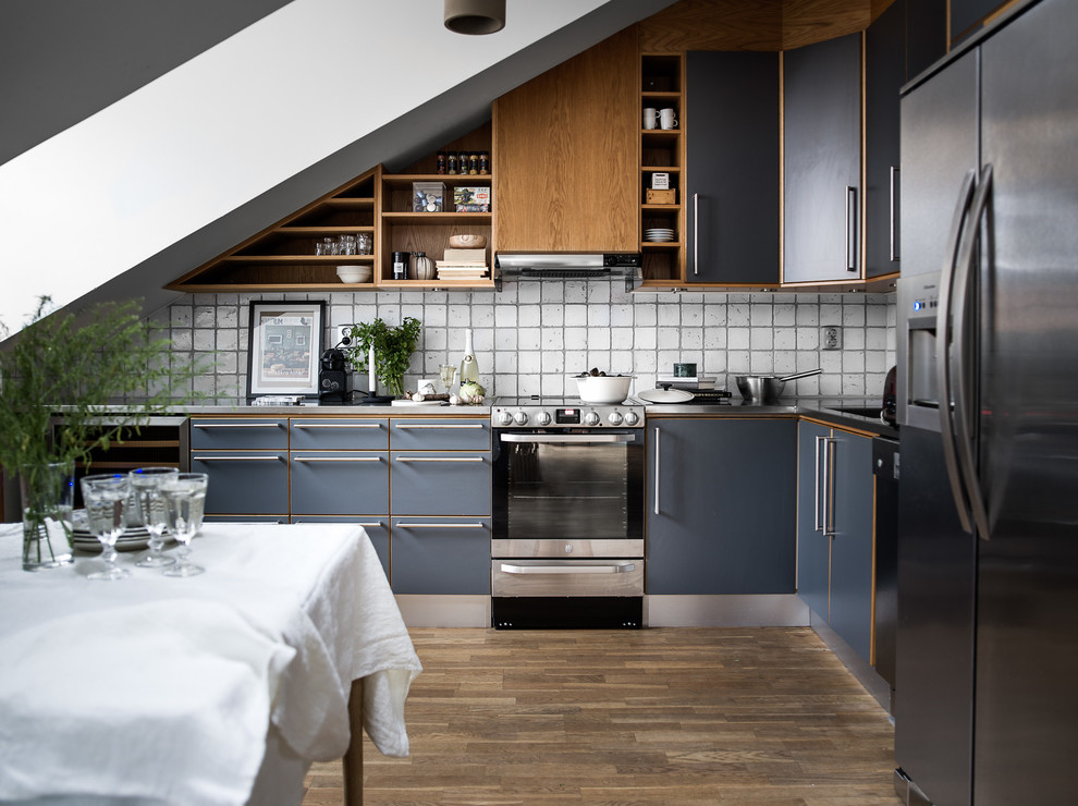 Photo of a mid-sized scandinavian l-shaped eat-in kitchen in Stockholm with flat-panel cabinets, blue cabinets, white splashback, no island, stainless steel appliances, medium hardwood floors and ceramic splashback.