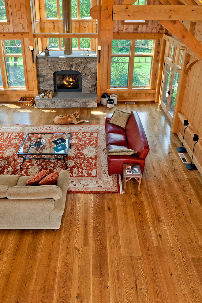 Photo of a country open concept living room in New York with medium hardwood floors, a standard fireplace, a stone fireplace surround and no tv.