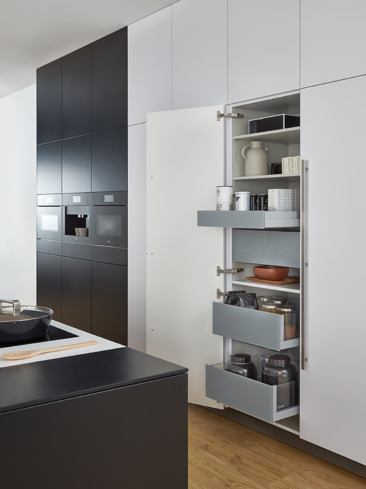 Inspiration for an expansive modern single-wall eat-in kitchen in New York with an undermount sink, flat-panel cabinets, black cabinets, solid surface benchtops, black appliances, light hardwood floors and with island.