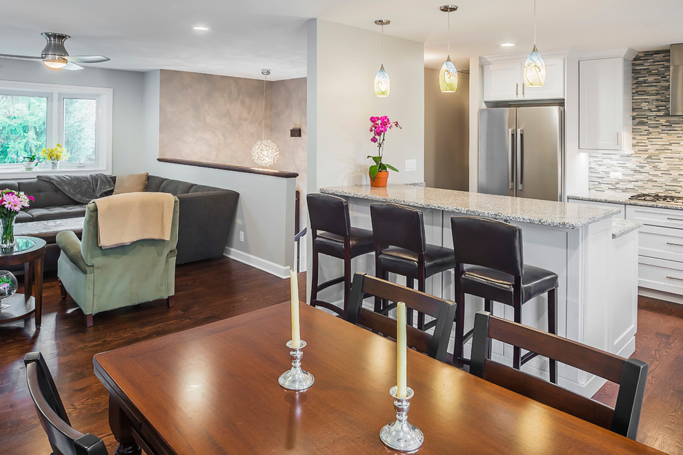 Example of a mid-sized transitional u-shaped medium tone wood floor eat-in kitchen design in Chicago with a farmhouse sink, recessed-panel cabinets, white cabinets, granite countertops, gray backsplash, glass tile backsplash, stainless steel appliances and an island