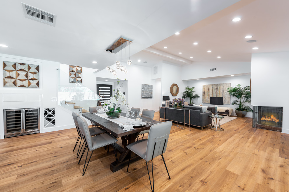 Large contemporary open plan dining in Los Angeles with white walls, a corner fireplace, a brick fireplace surround, medium hardwood floors and brown floor.