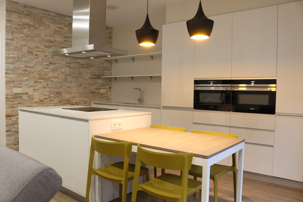 This is an example of a mid-sized contemporary single-wall open plan kitchen in Bilbao with flat-panel cabinets, white cabinets, marble benchtops, white splashback, metal splashback, stainless steel appliances, light hardwood floors and with island.