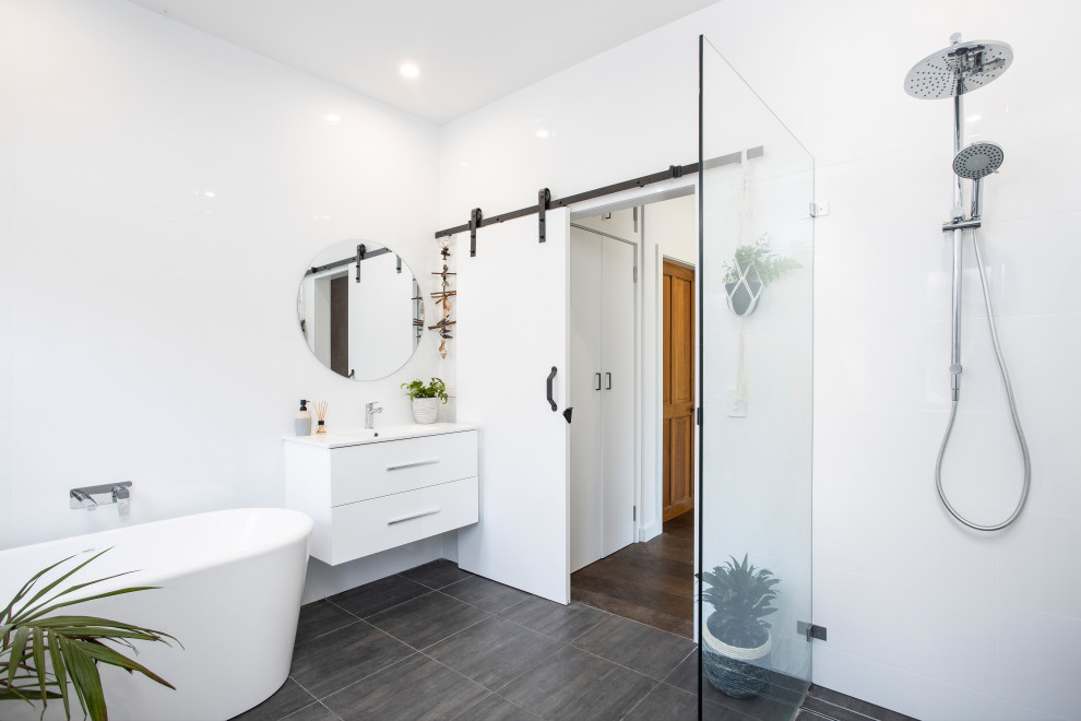 This is an example of a mid-sized contemporary master bathroom in Sydney with white cabinets, a freestanding tub, an open shower, white tile, ceramic tile, white walls, ceramic floors, an integrated sink, solid surface benchtops, grey floor, an open shower, white benchtops and flat-panel cabinets.