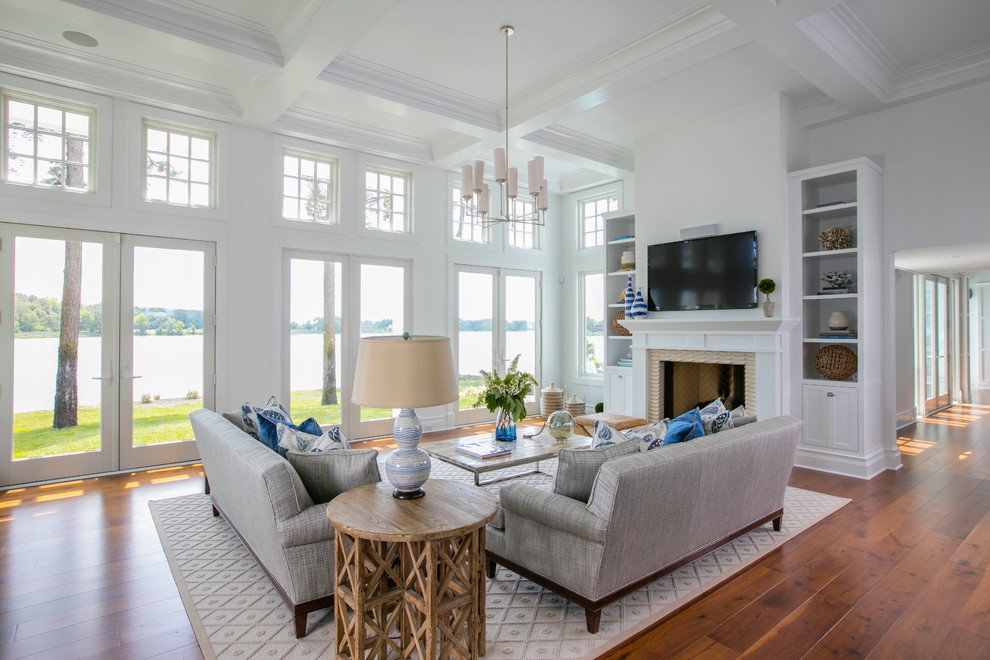 Photo of a mid-sized beach style open concept family room in Baltimore with white walls, medium hardwood floors, a standard fireplace, a wall-mounted tv and brown floor.