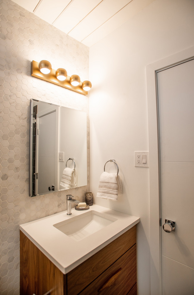 This is an example of a mid-sized contemporary master bathroom in Denver with flat-panel cabinets, medium wood cabinets, a drop-in tub, a shower/bathtub combo, a one-piece toilet, white tile, subway tile, white walls, mosaic tile floors, an undermount sink, engineered quartz benchtops, multi-coloured floor, a hinged shower door and white benchtops.