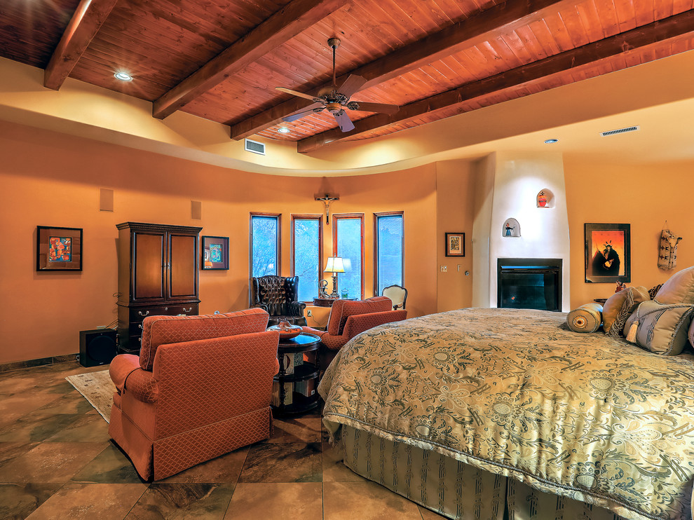 Photo of a mid-sized master bedroom in Albuquerque with yellow walls, slate floors, a standard fireplace, a plaster fireplace surround and multi-coloured floor.