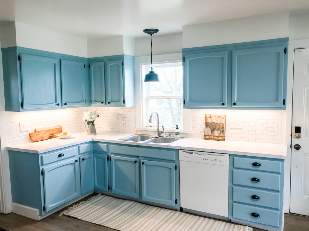 This is an example of a rural l-shaped kitchen/diner in San Francisco with a double-bowl sink, raised-panel cabinets, blue cabinets, laminate countertops, white splashback, metro tiled splashback, white appliances, vinyl flooring, no island, brown floors and multicoloured worktops.