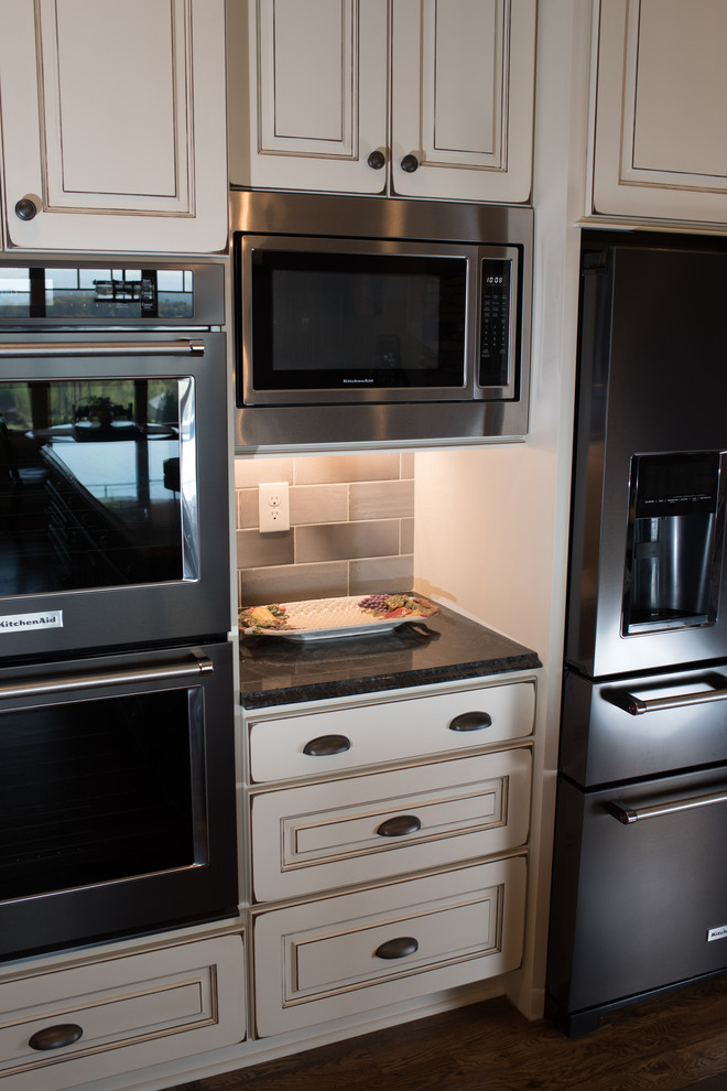 Eat-in kitchen - large rustic l-shaped dark wood floor and brown floor eat-in kitchen idea with a farmhouse sink, raised-panel cabinets, granite countertops, gray backsplash, ceramic backsplash, black appliances, an island and white cabinets