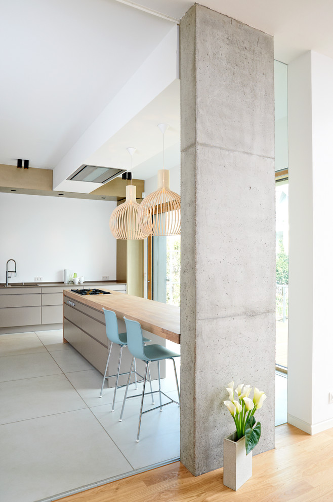 Inspiration for a large contemporary single-wall eat-in kitchen in Hamburg with an undermount sink, flat-panel cabinets, grey cabinets, wood benchtops, white splashback, panelled appliances, concrete floors and a peninsula.