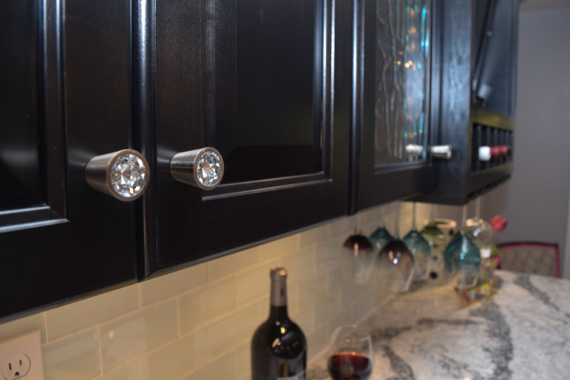 Transitional medium tone wood floor kitchen photo in Chicago with a farmhouse sink, raised-panel cabinets, black cabinets, quartz countertops, white backsplash, glass tile backsplash, stainless steel appliances and an island