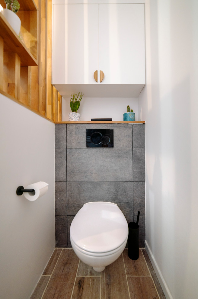 Idéer för ett mellanstort minimalistiskt brun toalett, med luckor med profilerade fronter, en toalettstol med hel cisternkåpa, grå kakel, vita väggar, ett nedsänkt handfat, träbänkskiva, brunt golv och vita skåp