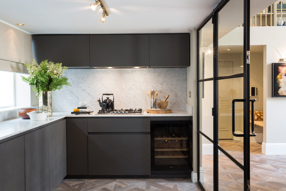 Small contemporary l-shaped separate kitchen in London with flat-panel cabinets, black cabinets, grey splashback, stone slab splashback, light hardwood floors and no island.