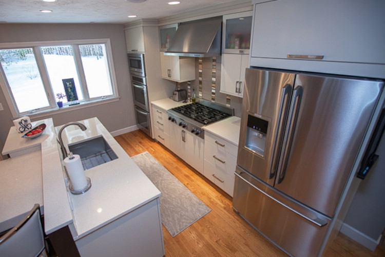 This is an example of a large contemporary single-wall eat-in kitchen in Boston with an undermount sink, recessed-panel cabinets, grey cabinets, quartz benchtops, grey splashback, glass sheet splashback, stainless steel appliances, medium hardwood floors and multiple islands.