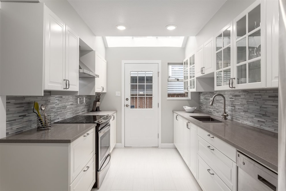 This is an example of a mid-sized contemporary galley separate kitchen in Vancouver with an undermount sink, raised-panel cabinets, white cabinets, solid surface benchtops, grey splashback, glass tile splashback, stainless steel appliances, ceramic floors, no island and white floor.