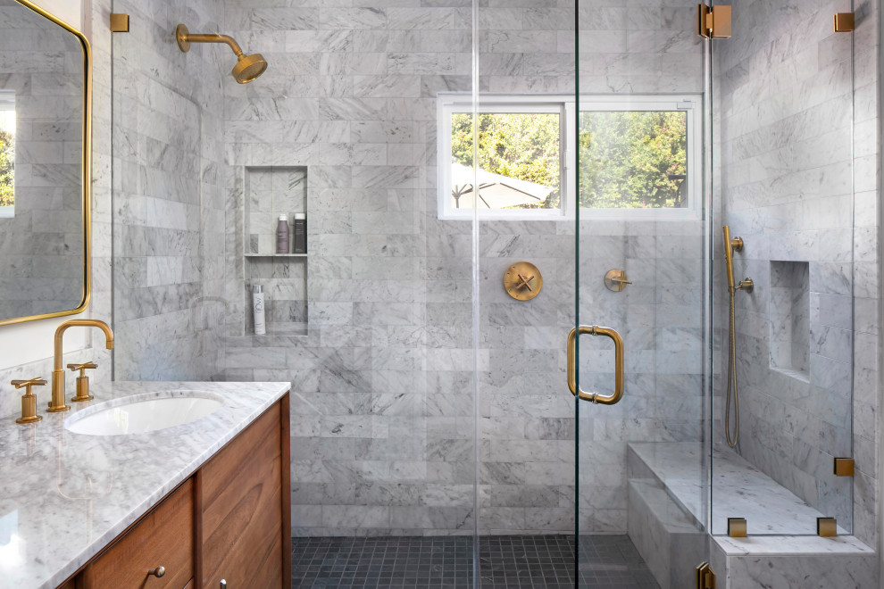 Photo of a mid-sized transitional master bathroom in Los Angeles with flat-panel cabinets, medium wood cabinets, an alcove shower, a wall-mount toilet, multi-coloured tile, marble, white walls, porcelain floors, an undermount sink, marble benchtops, black floor, a hinged shower door, multi-coloured benchtops, a shower seat, a double vanity and a freestanding vanity.