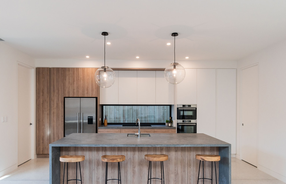 Inspiration for a contemporary galley kitchen in Melbourne with an undermount sink, flat-panel cabinets, medium wood cabinets, window splashback, stainless steel appliances, bamboo floors, with island, beige floor and grey benchtop.