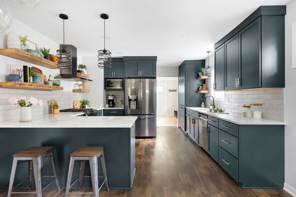 Photo of a mid-sized transitional u-shaped eat-in kitchen in Minneapolis with an undermount sink, shaker cabinets, blue cabinets, quartz benchtops, grey splashback, ceramic splashback, stainless steel appliances, vinyl floors, a peninsula, brown floor and white benchtop.