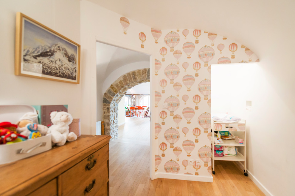 Cette photo montre une petite chambre de bébé neutre chic avec parquet clair, un plafond voûté et du papier peint.