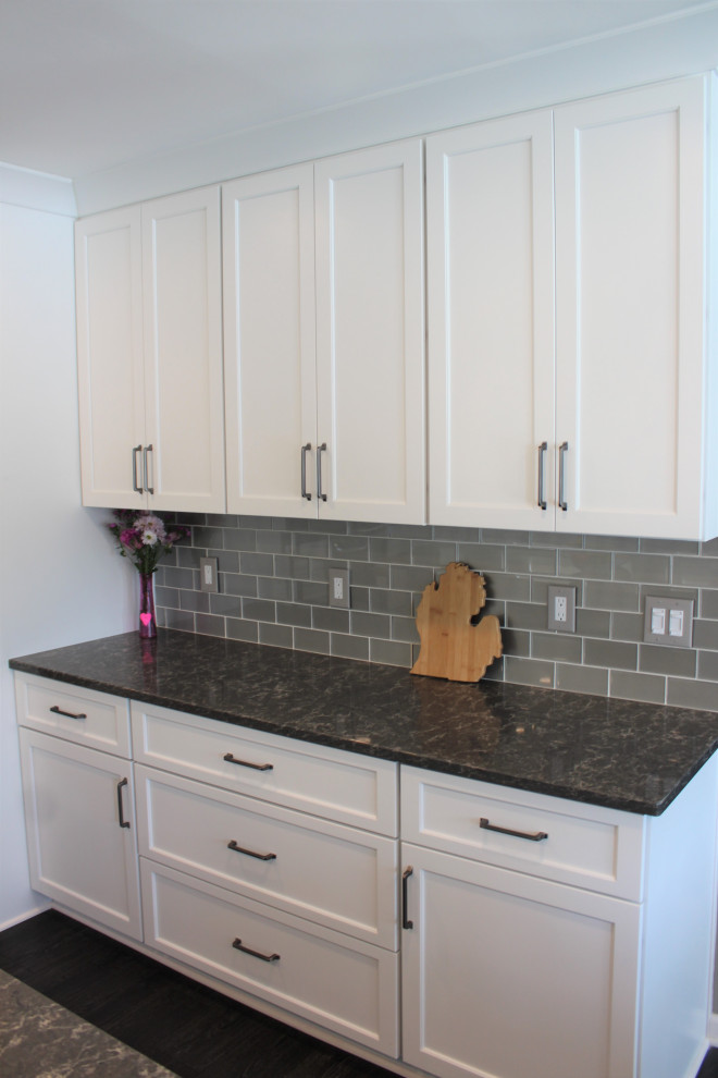Inredning av ett stort grå grått kök, med en undermonterad diskho, luckor med infälld panel, vita skåp, bänkskiva i kvarts, grönt stänkskydd, stänkskydd i glaskakel, rostfria vitvaror, laminatgolv, en köksö och grått golv
