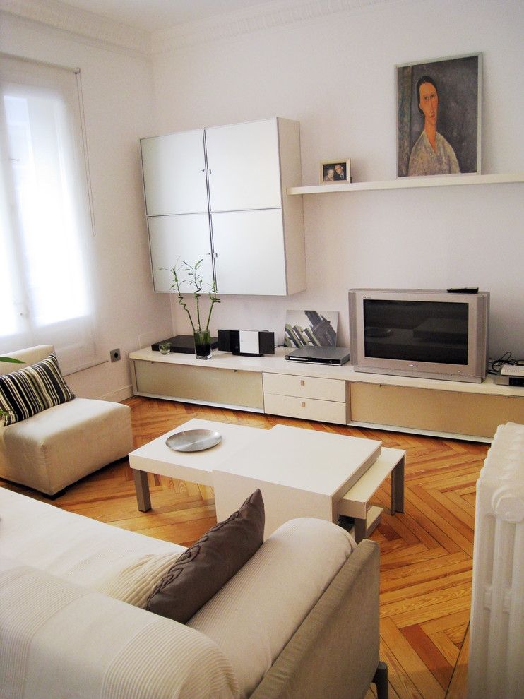 This is an example of a small contemporary formal enclosed living room in Madrid with white walls, medium hardwood floors, no fireplace and a freestanding tv.