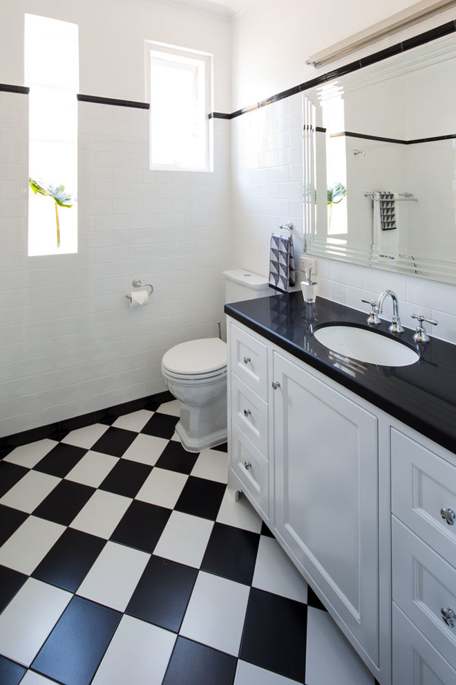 Inspiration for a mid-sized traditional 3/4 bathroom in Melbourne with shaker cabinets, white cabinets, a drop-in tub, a two-piece toilet, black and white tile, ceramic tile, white walls, ceramic floors, an undermount sink, granite benchtops and black floor.