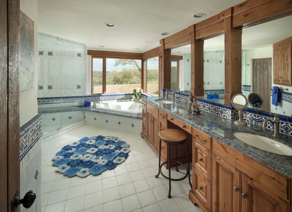 Photo of a large mediterranean master bathroom in Phoenix with an undermount sink, raised-panel cabinets, a corner tub, a corner shower, blue tile, terra-cotta floors, a two-piece toilet, white walls, granite benchtops, dark wood cabinets and blue benchtops.