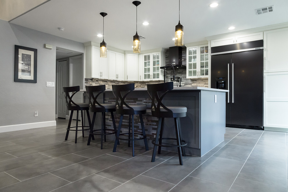 Example of a mid-sized transitional l-shaped porcelain tile and gray floor open concept kitchen design in Phoenix with an undermount sink, shaker cabinets, white cabinets, quartz countertops, gray backsplash, glass tile backsplash, black appliances, an island and gray countertops