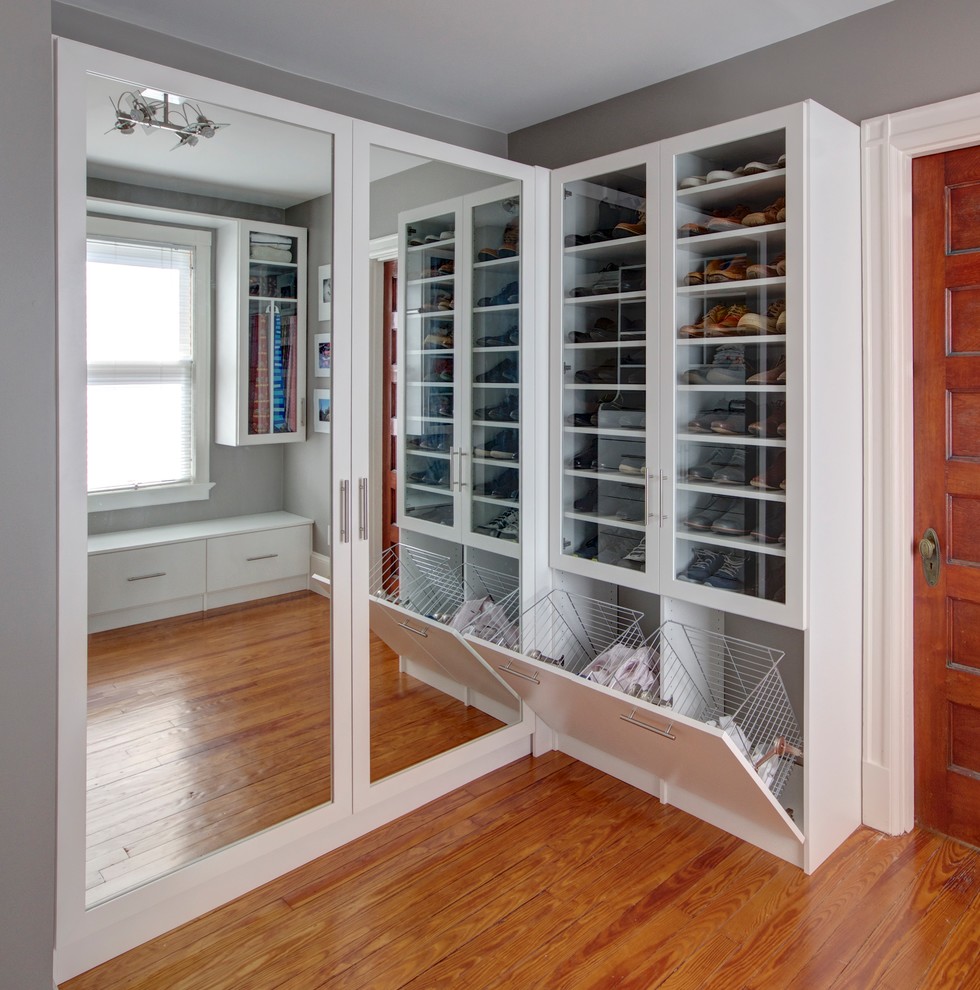 Inspiration for a mid-sized transitional gender-neutral walk-in wardrobe in New York with glass-front cabinets, white cabinets, medium hardwood floors and brown floor.