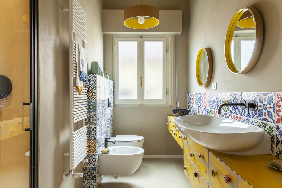 Пример оригинального дизайна: узкая и длинная ванная комната среднего размера в средиземноморском стиле с плоскими фасадами, желтыми фасадами, инсталляцией, разноцветной плиткой, керамической плиткой, разноцветными стенами, бетонным полом, душевой кабиной, настольной раковиной, столешницей из дерева, душем с распашными дверями, желтой столешницей, тумбой под одну раковину и встроенной тумбой