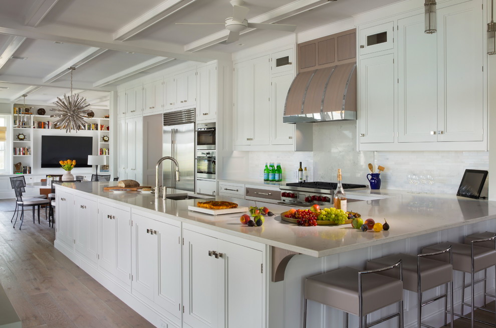 Photo of a large beach style u-shaped open plan kitchen in New York with an undermount sink, white cabinets, granite benchtops, white splashback, stone tile splashback, stainless steel appliances, medium hardwood floors, a peninsula and recessed-panel cabinets.