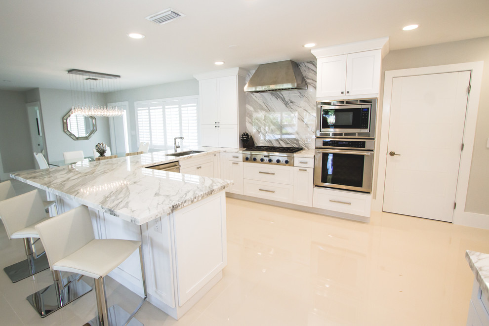 Photo of a large contemporary l-shaped separate kitchen in Miami with an undermount sink, shaker cabinets, white cabinets, marble benchtops, red splashback, marble splashback, stainless steel appliances, porcelain floors, a peninsula, beige floor and white benchtop.