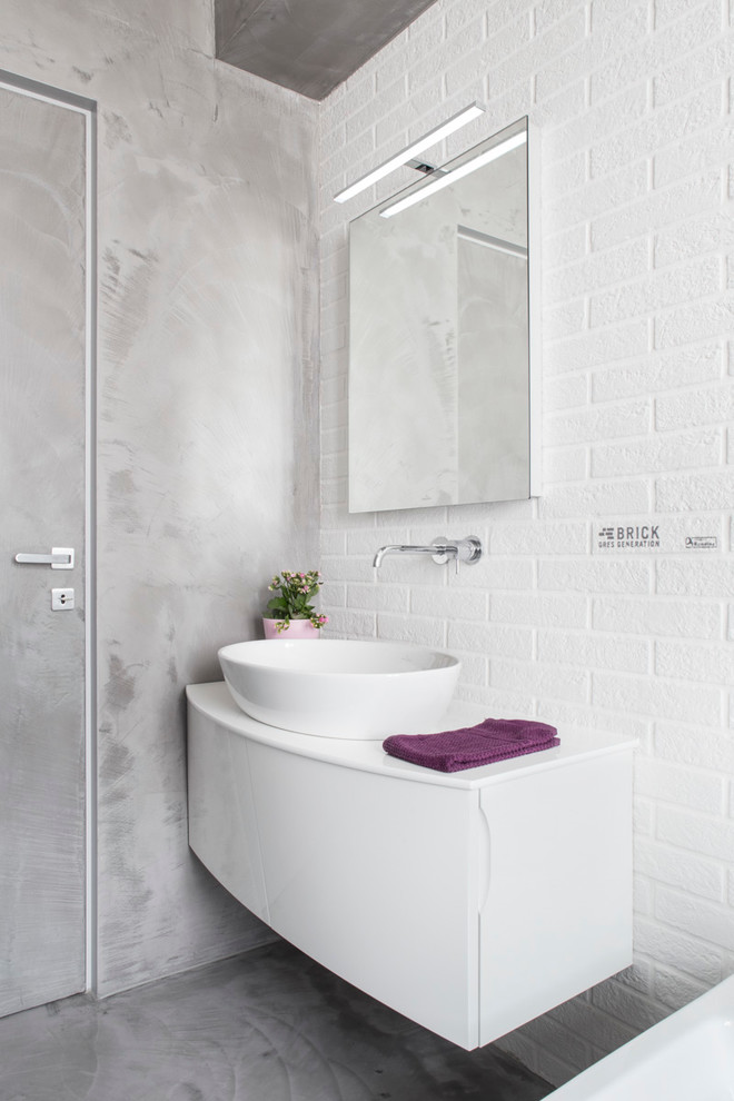 Design ideas for a small industrial powder room in Milan with flat-panel cabinets, white cabinets, white tile, grey walls, concrete floors and a vessel sink.