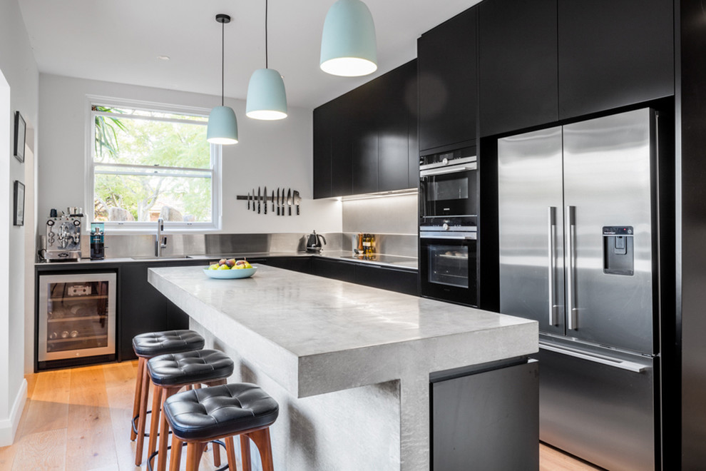 This is an example of a contemporary l-shaped eat-in kitchen in Sydney with black cabinets, concrete benchtops, metallic splashback, with island, grey benchtop, flat-panel cabinets, stainless steel appliances, medium hardwood floors and brown floor.
