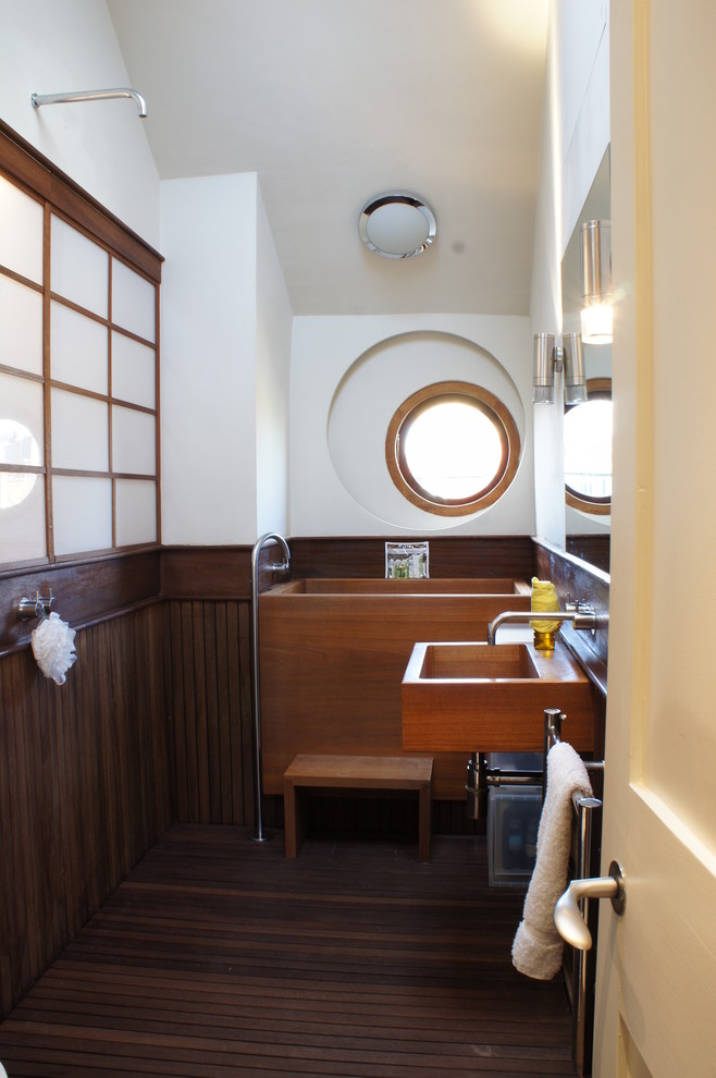 This is an example of an eclectic bathroom in London with a wall-mount sink, a japanese tub, an open shower, white walls, medium hardwood floors and an open shower.