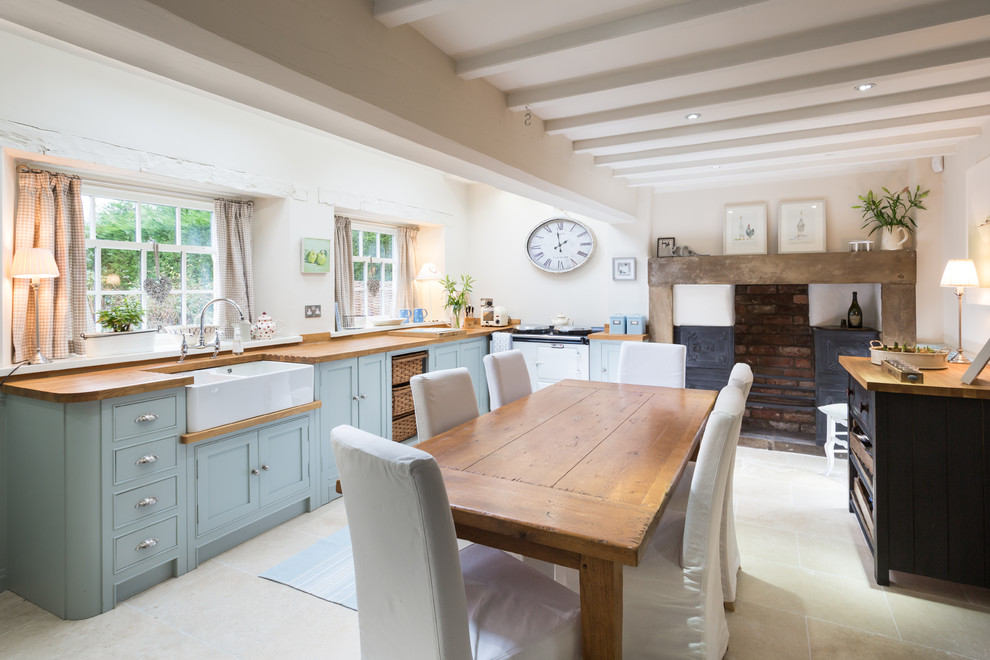 Mid-sized country l-shaped eat-in kitchen in Other with a farmhouse sink, shaker cabinets, blue cabinets, wood benchtops, white splashback, white appliances, travertine floors and no island.