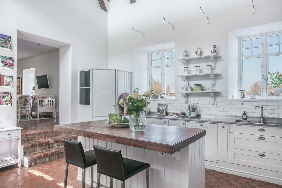 Inspiration for a large traditional single-wall eat-in kitchen in Malmo with wood benchtops, white splashback, brick floors, with island, red floor, a double-bowl sink, shaker cabinets, white cabinets, subway tile splashback and brown benchtop.